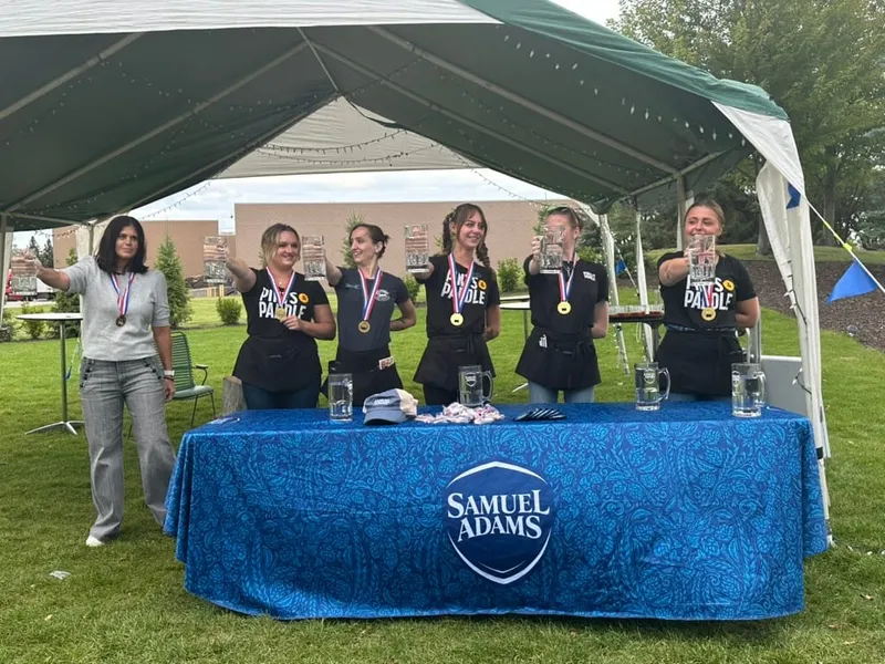 Five staff in Pints & Paddle shirts wearing medals behind the Samuel Adams table under the tent