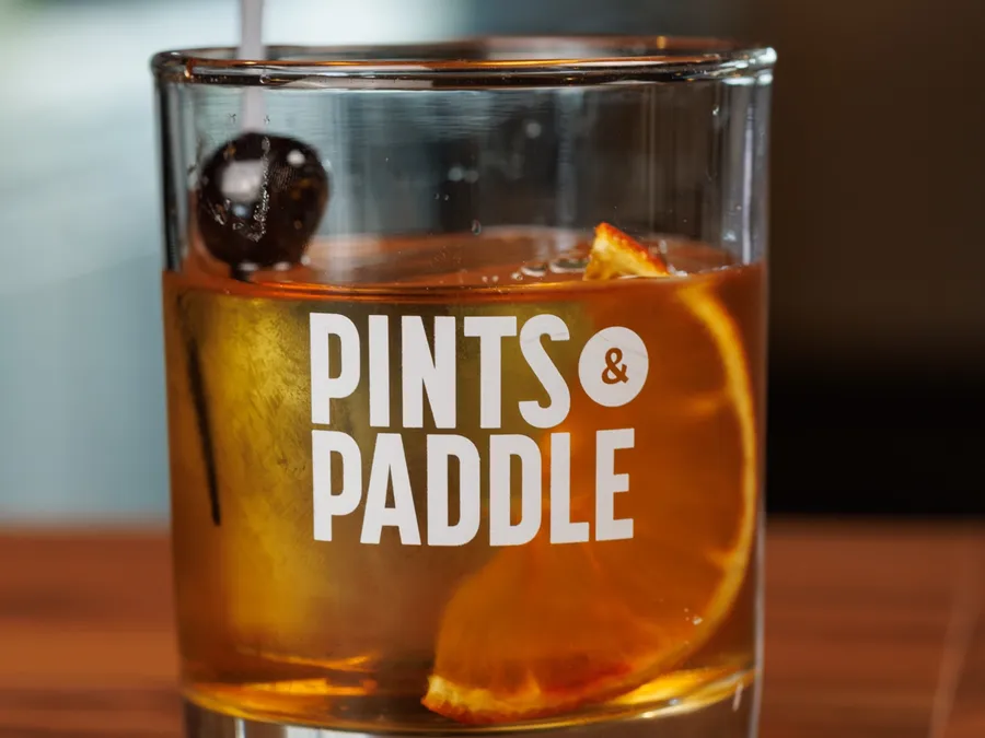 An Old Fashioned in a Pints & Paddle rocks glass with a large clear ice cube, orange wheel and cherry