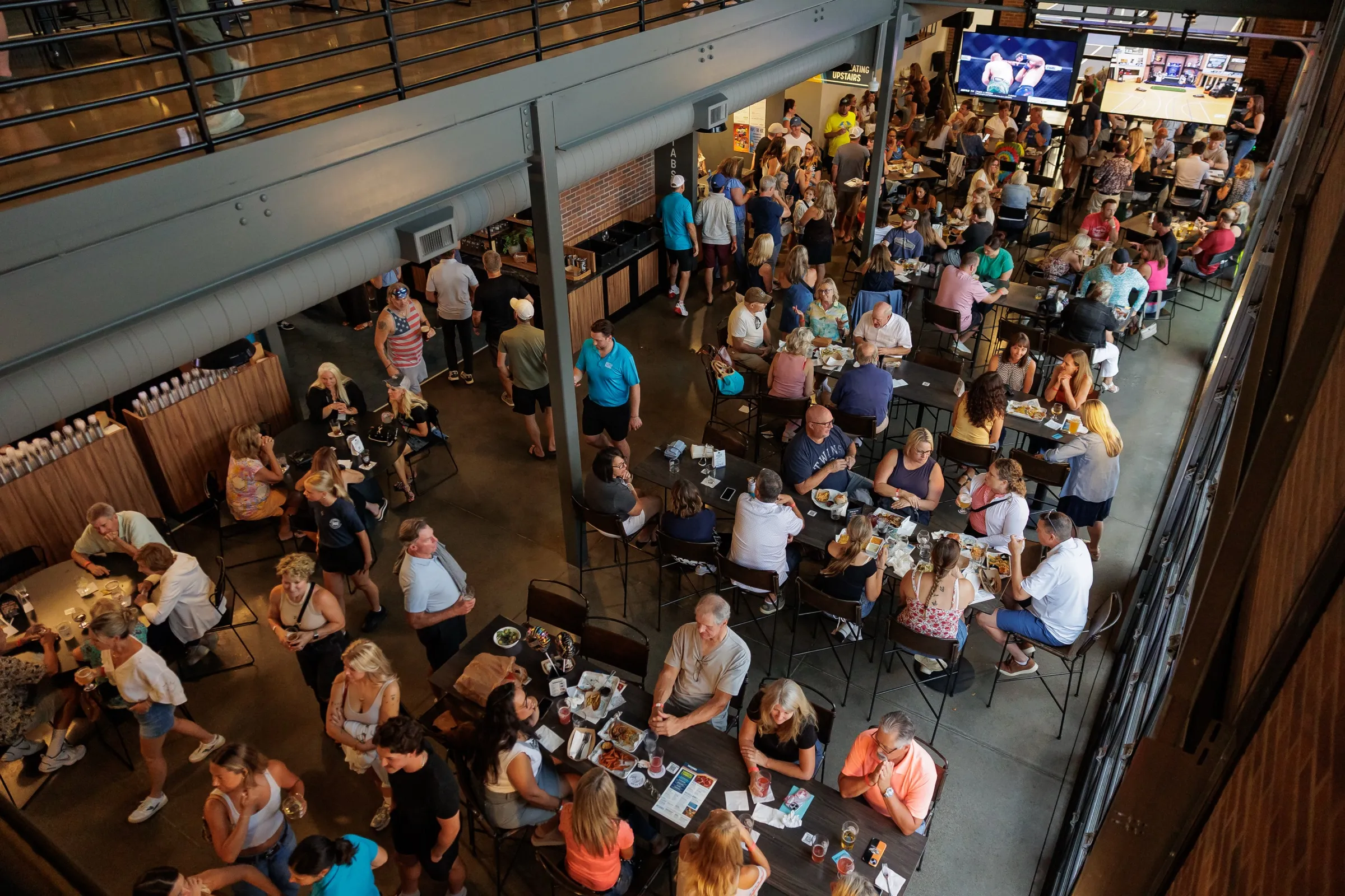 Looking down from the mezzanine on a packed main-level taproom, every long table full