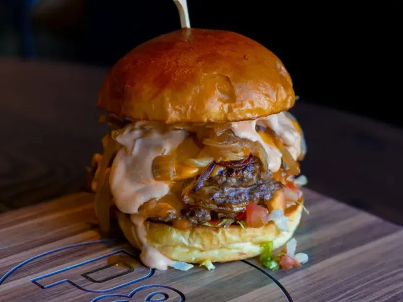 Paddy's Burger with melted cheese, grilled onions, lettuce, tomato and Paddy's sauce on a branded wooden board