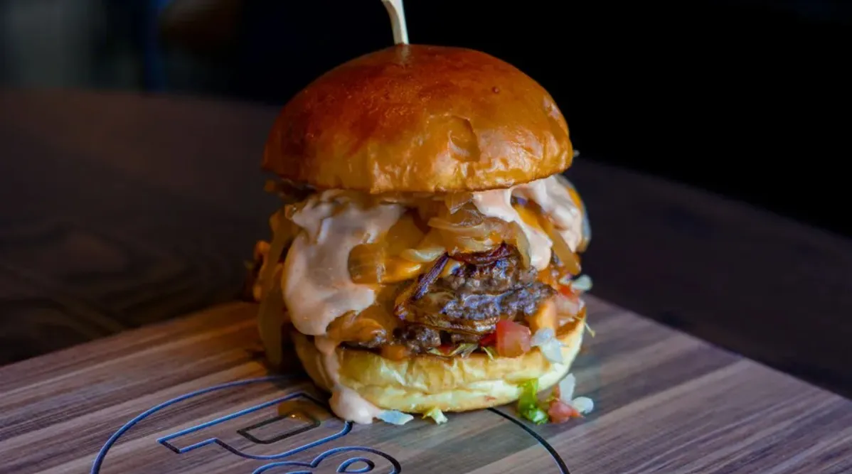 Paddy's Burger with melted cheese, grilled onions, lettuce, tomato and Paddy's sauce on a branded wooden board