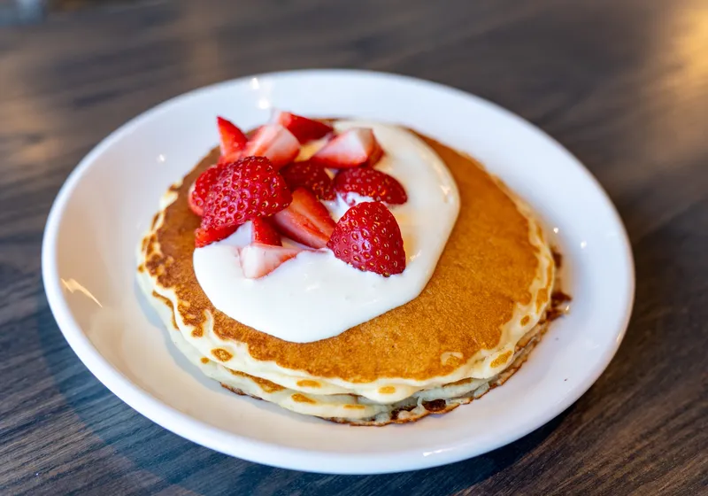 A short stack of pancakes topped with whipped cream cheese and sliced strawberries