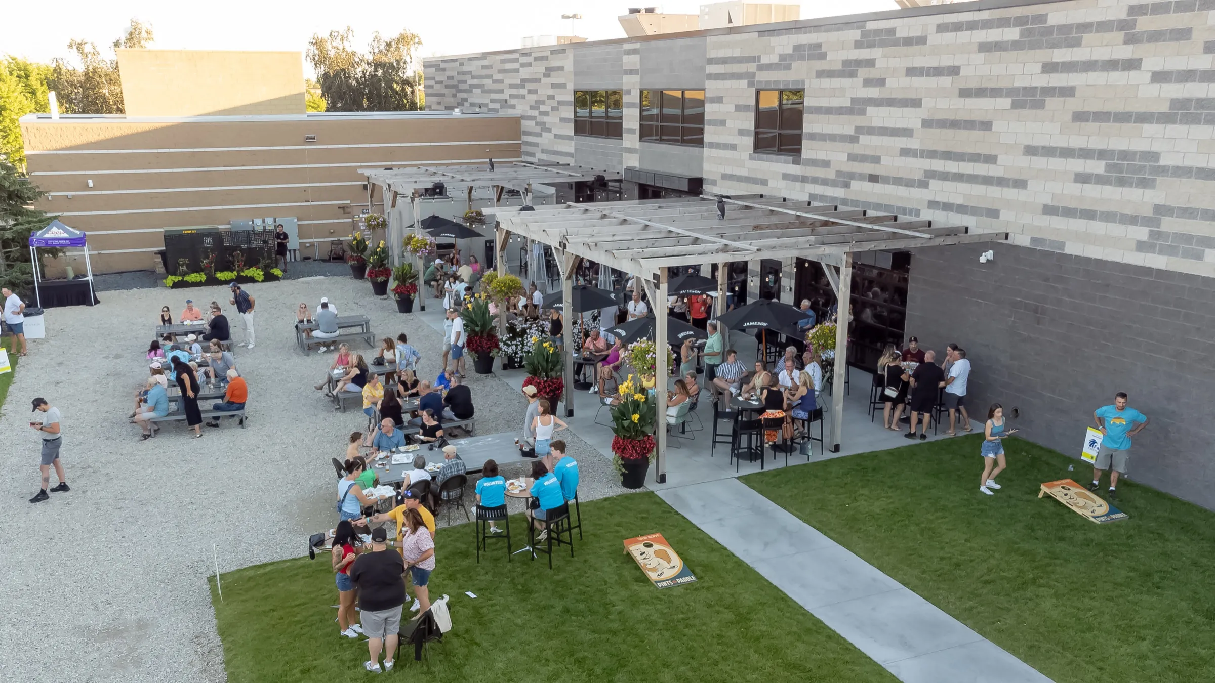 Golden-hour view of the patio, with guests under the pergola and picnic tables beside the lawn