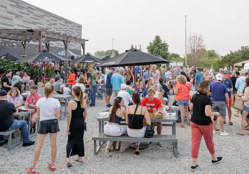 A busy evening on the gravel patio under pergolas and string lights, with the building behind