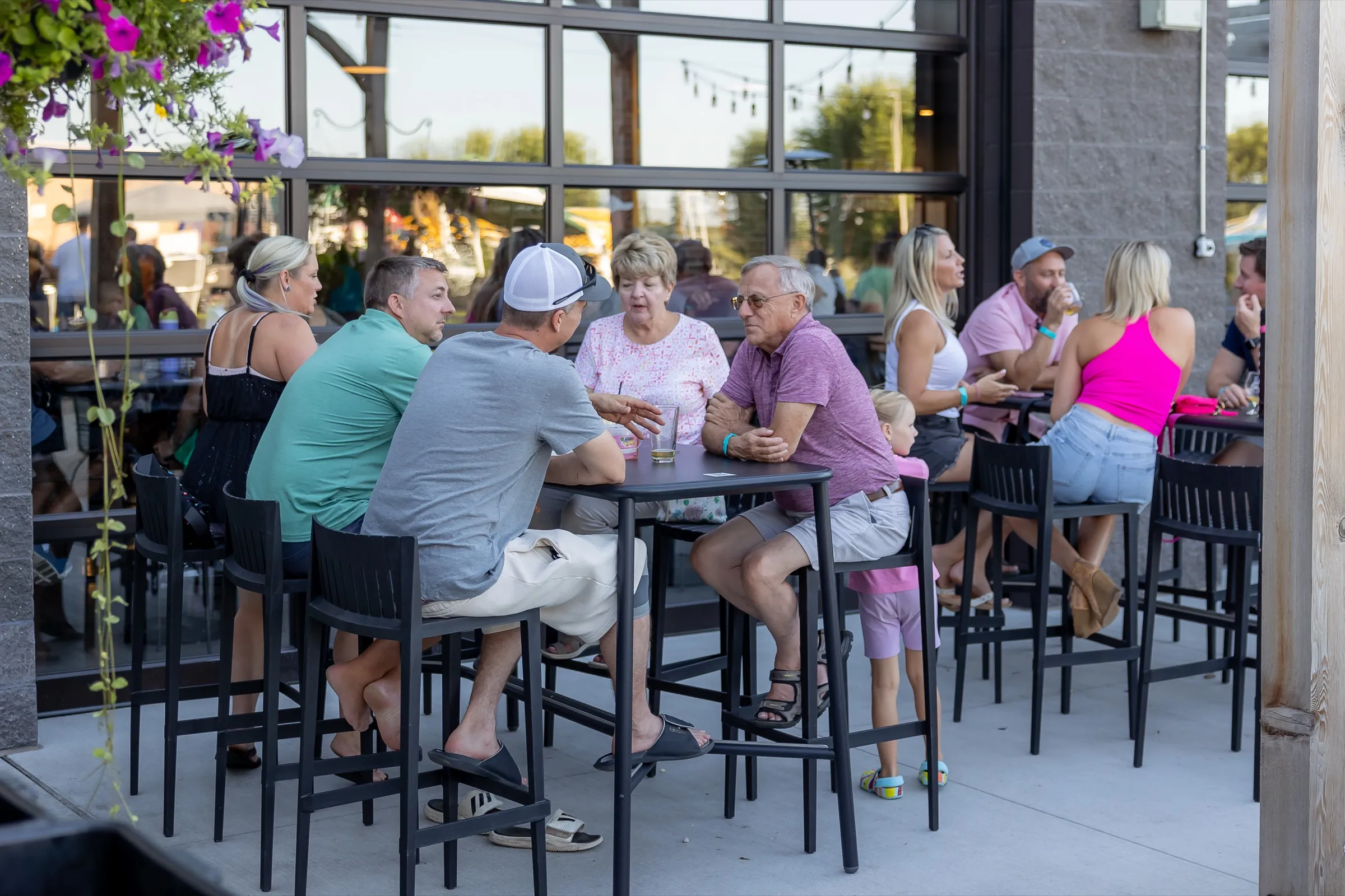 Friends at a high-top table on the patio in warm evening light, the glass garage doors and string lights behind them