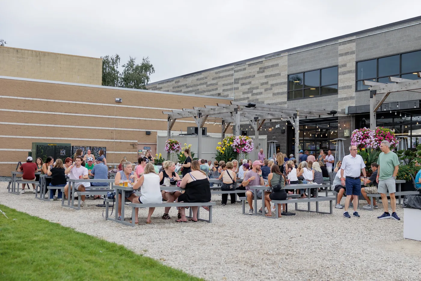The patio on an overcast day: picnic tables full of guests under the pergolas, with the building and open garage doors behind