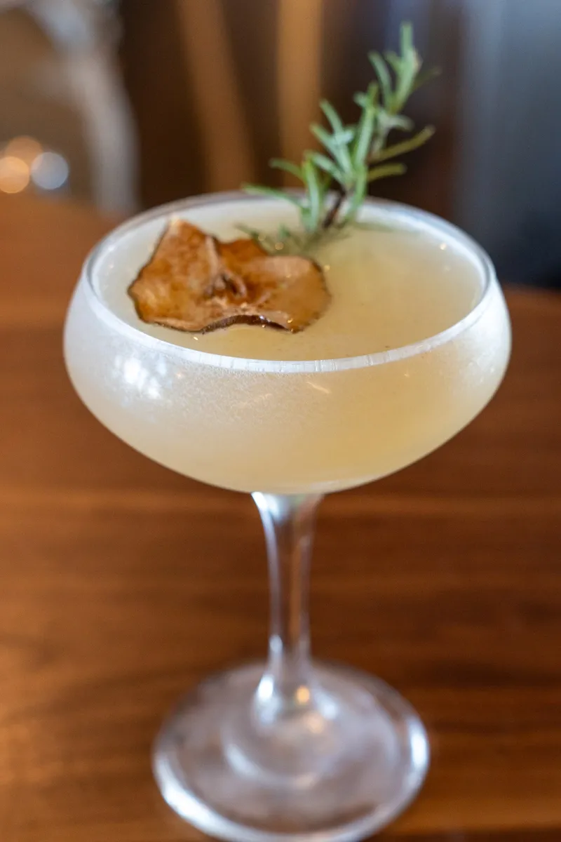 A pale Pear Martini in a coupe, garnished with a dried fruit slice and a sprig of rosemary.