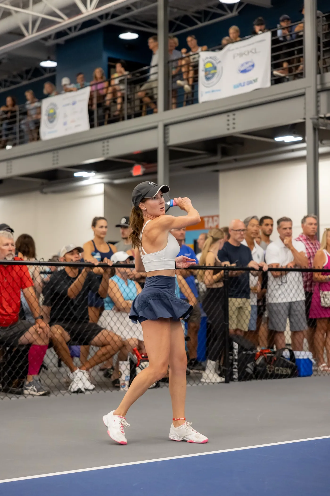 A player follows through on a backhand with a dense crowd at the rail and on the mezzanine behind her