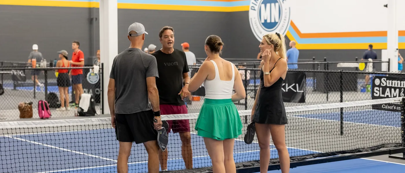 Four players chatting at the net beneath the Pints & Paddle logo wall
