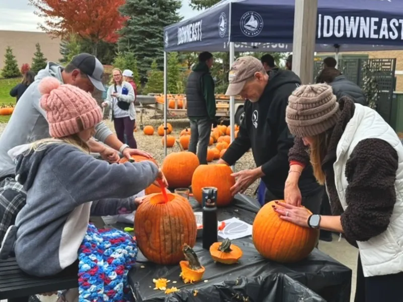 A family scooping out pumpkins at a table under the Downeast Cider tent