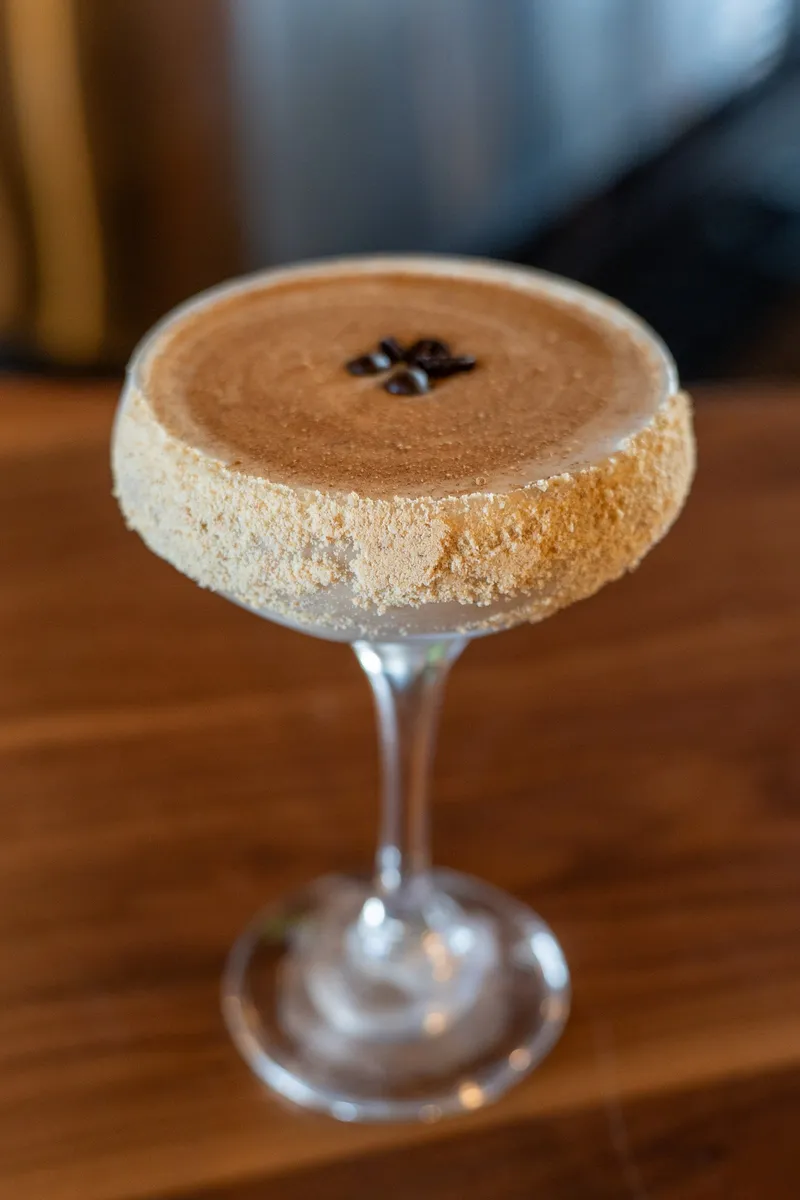 A Pumpkin Pie Espresso Martini in a coupe with a graham-cracker rim and coffee beans on the foam.