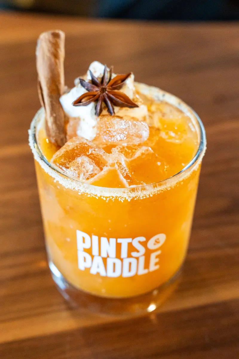 An orange Pumpkin Pie Smash over ice in a Pints & Paddle rocks glass, garnished with a cinnamon stick and star anise.