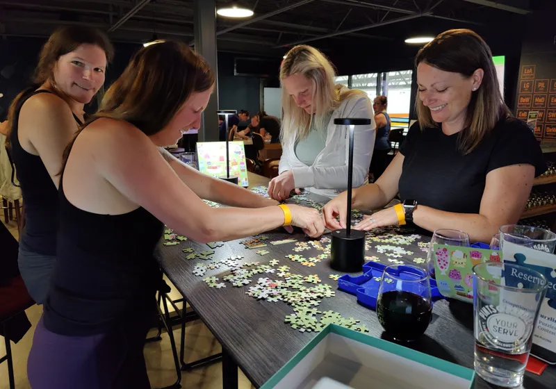 Four women sorting jigsaw pieces at a high-top table during a puzzle competition