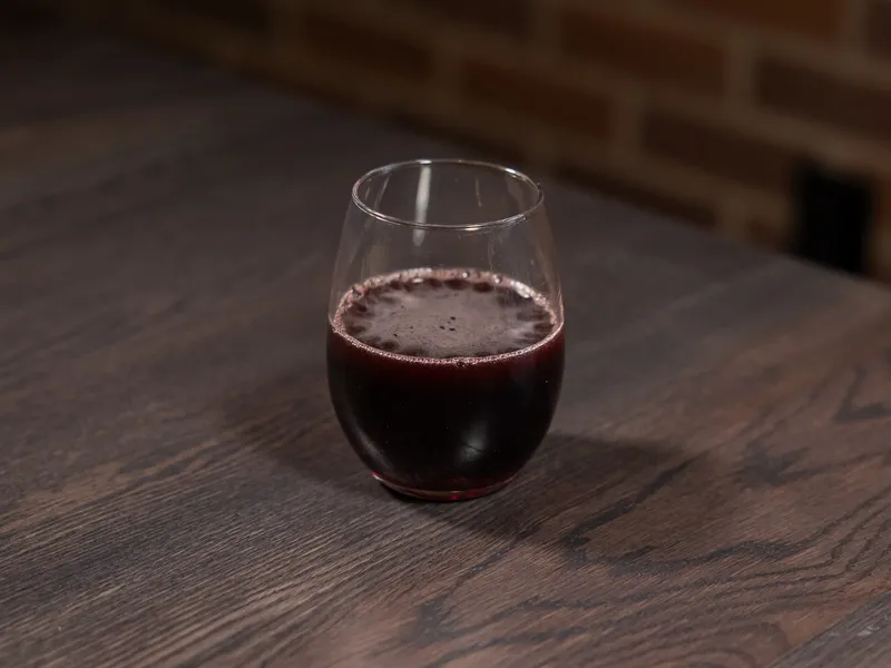 A stemless glass of red wine on a dark wood table in front of a brick wall