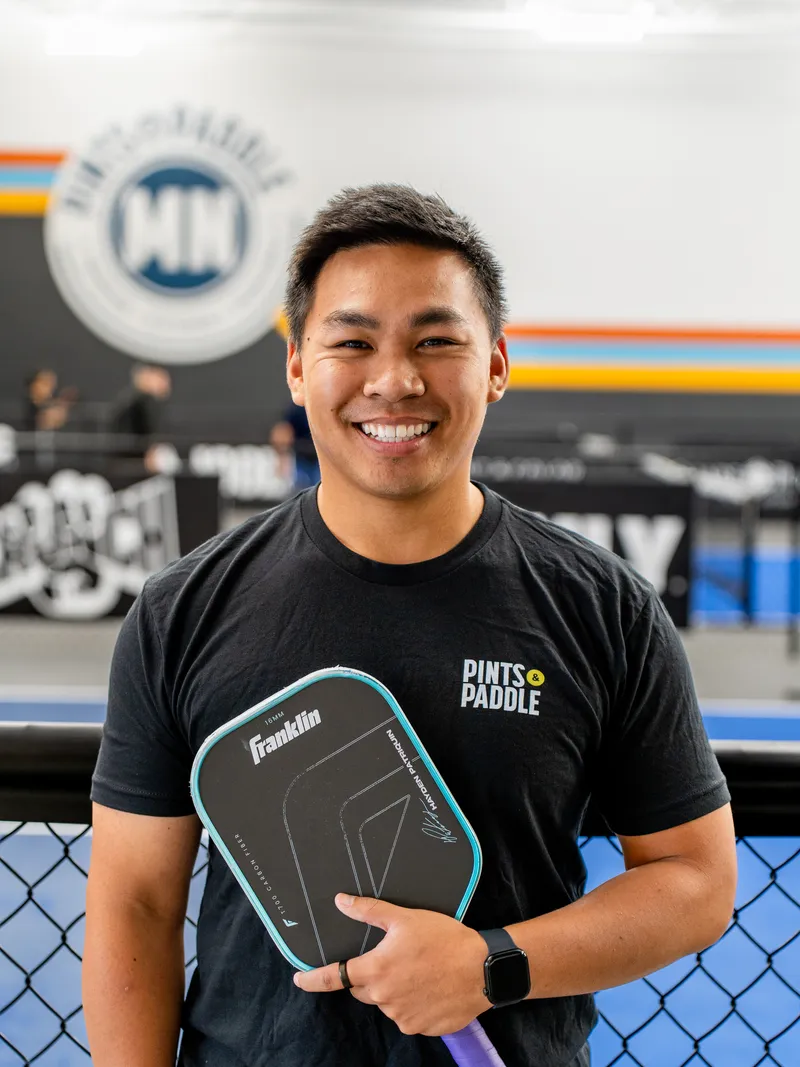Roman Pham smiling and holding a paddle on the courts at Pints & Paddle