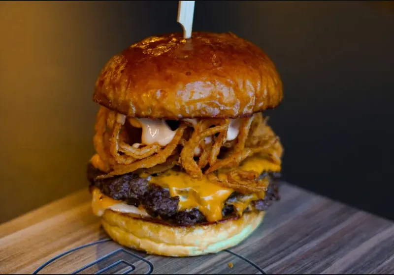 Royale Burger with Cheese topped with crispy onion strings and sauce on a branded wooden board