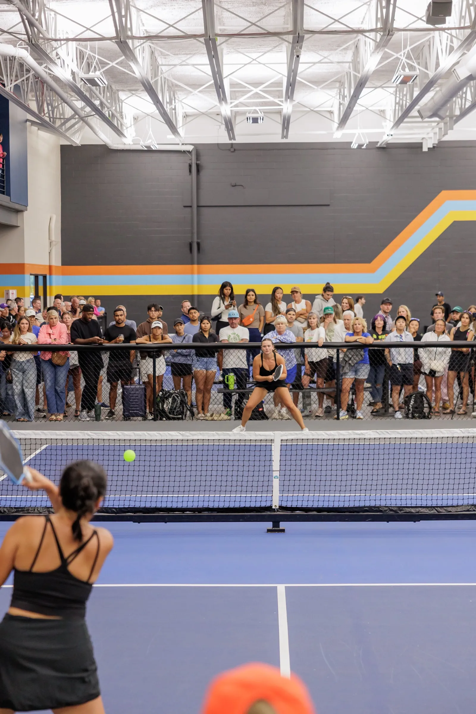 A player serves from the baseline while a packed crowd watches from the fence and the mezzanine above