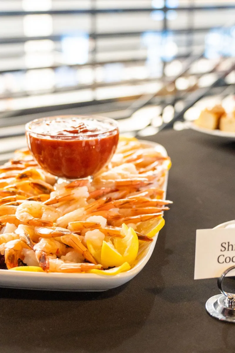 A shrimp cocktail platter with lemon wedges and a bowl of cocktail sauce on a black-draped buffet table
