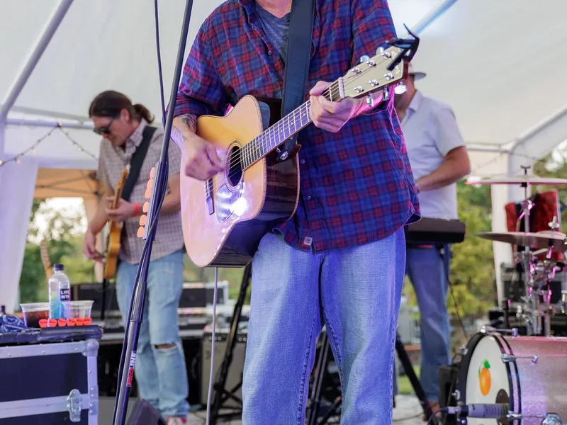 A singer-guitarist performs under the white stage tent on the lawn