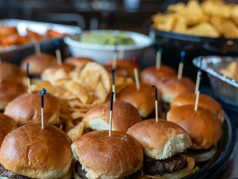 Cheeseburger sliders on brioche with toothpicks, the wider spread blurred behind