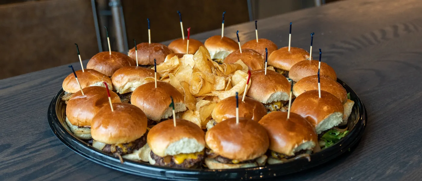 A round platter of cheeseburger sliders with a pile of house kettle chips in the center