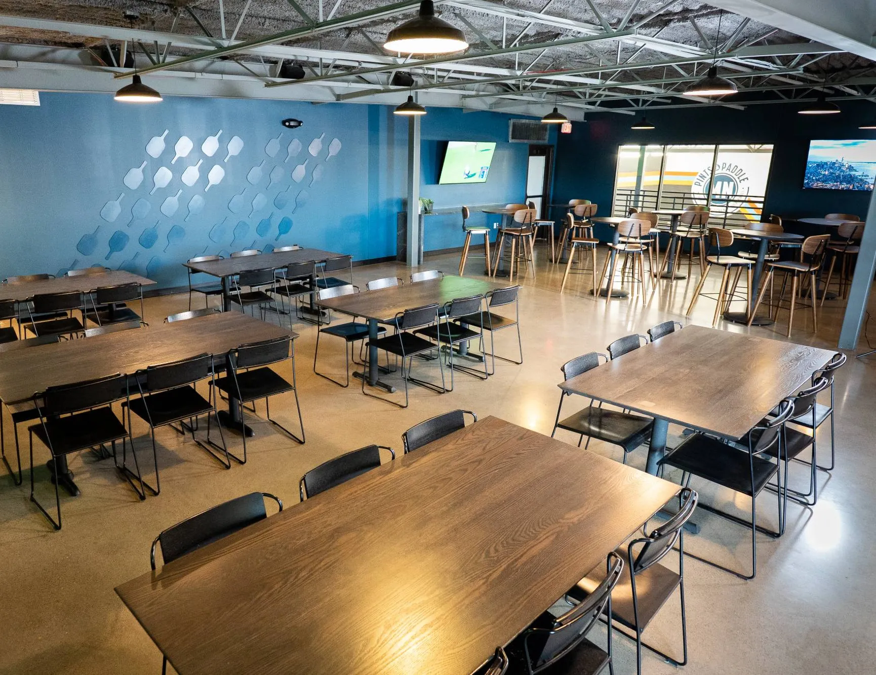 South mezzanine with long dining tables in front of the teal paddle-pattern wall and round high-top tables by the court windows