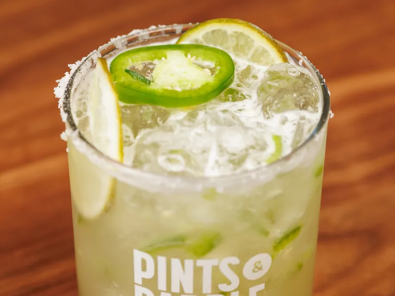 A spicy margarita with a salt rim, a jalapeño slice and a lime wheel in a Pints & Paddle logo glass
