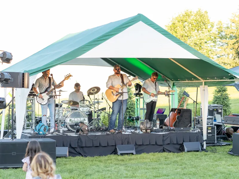 A four-piece band on the low stage under the green-and-white tent, a small child watching from the grass