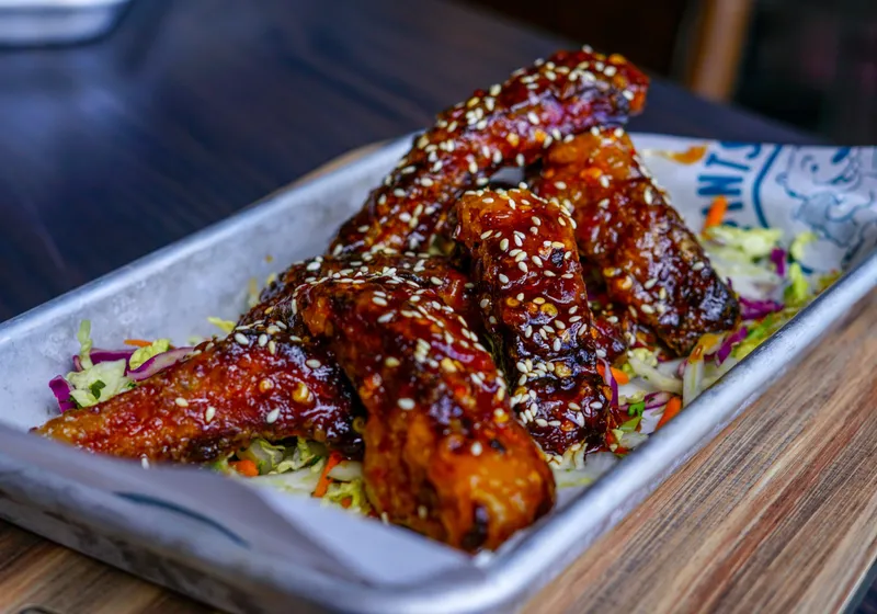 Glossy sesame-topped sticky ribs piled over slaw in a metal tray lined with branded paper