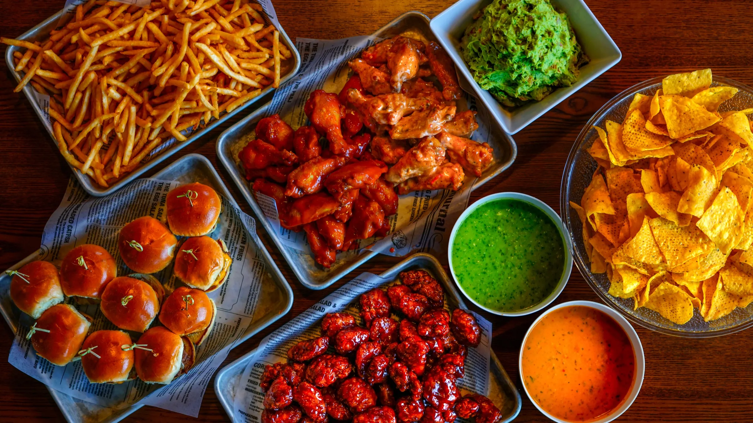 An overhead party spread of wings, fries, sliders, guacamole, chips and dips