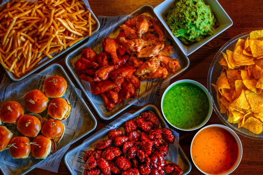 An overhead party spread of wings, fries, sliders, guacamole, chips and dips