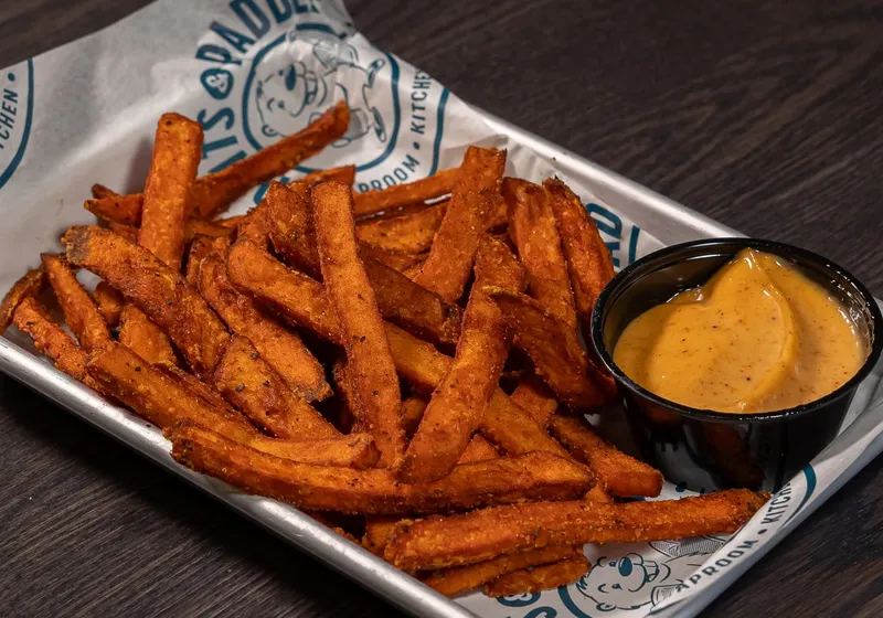 A metal tray of Cajun-seasoned sweet potato fries with a black cup of chipotle aioli on branded paper