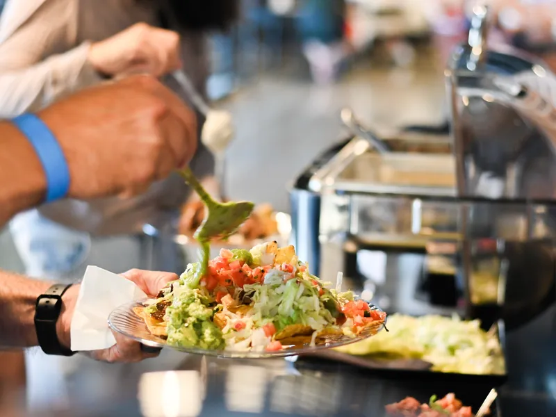 A guest spooning guacamole onto a plate of nachos at the taco bar, chafers behind
