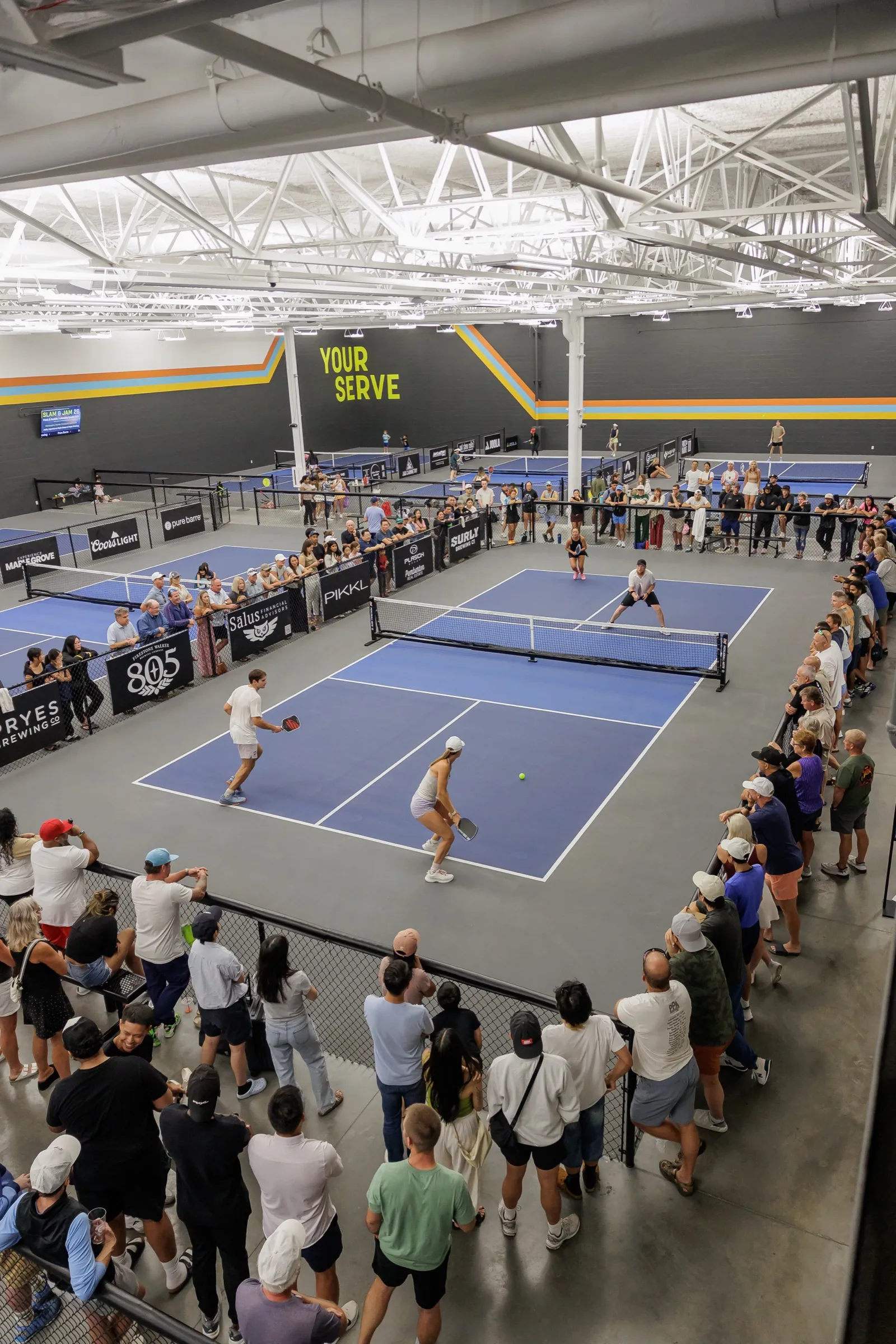 The championship court seen from the mezzanine, ringed by a standing crowd, with the Your Serve wall behind