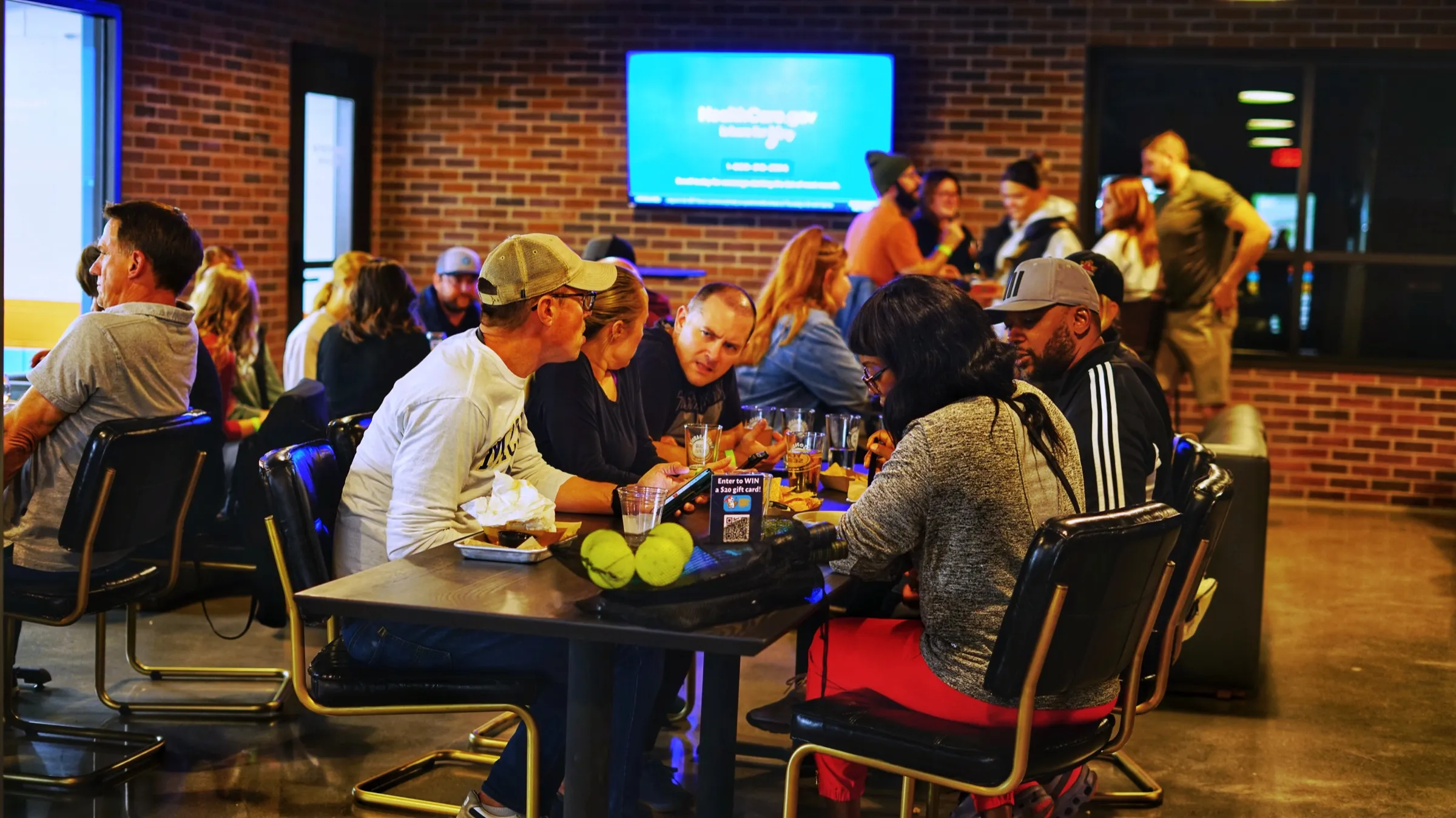 A trivia team gathered around a table in the brick-walled lounge, a big wall TV showing the question slide behind them
