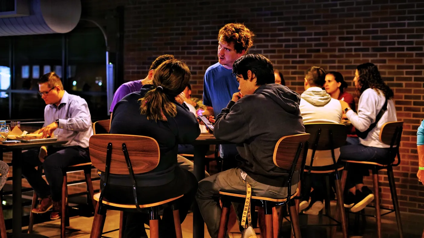 A trivia team huddled over an answer sheet at a table against a brick wall
