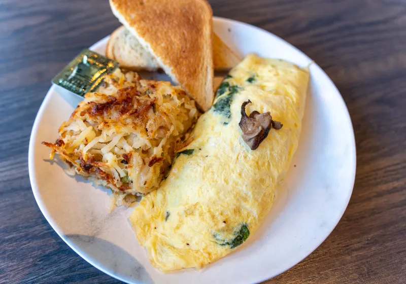A spinach and mushroom omelette with a crispy hash brown and two triangles of toast
