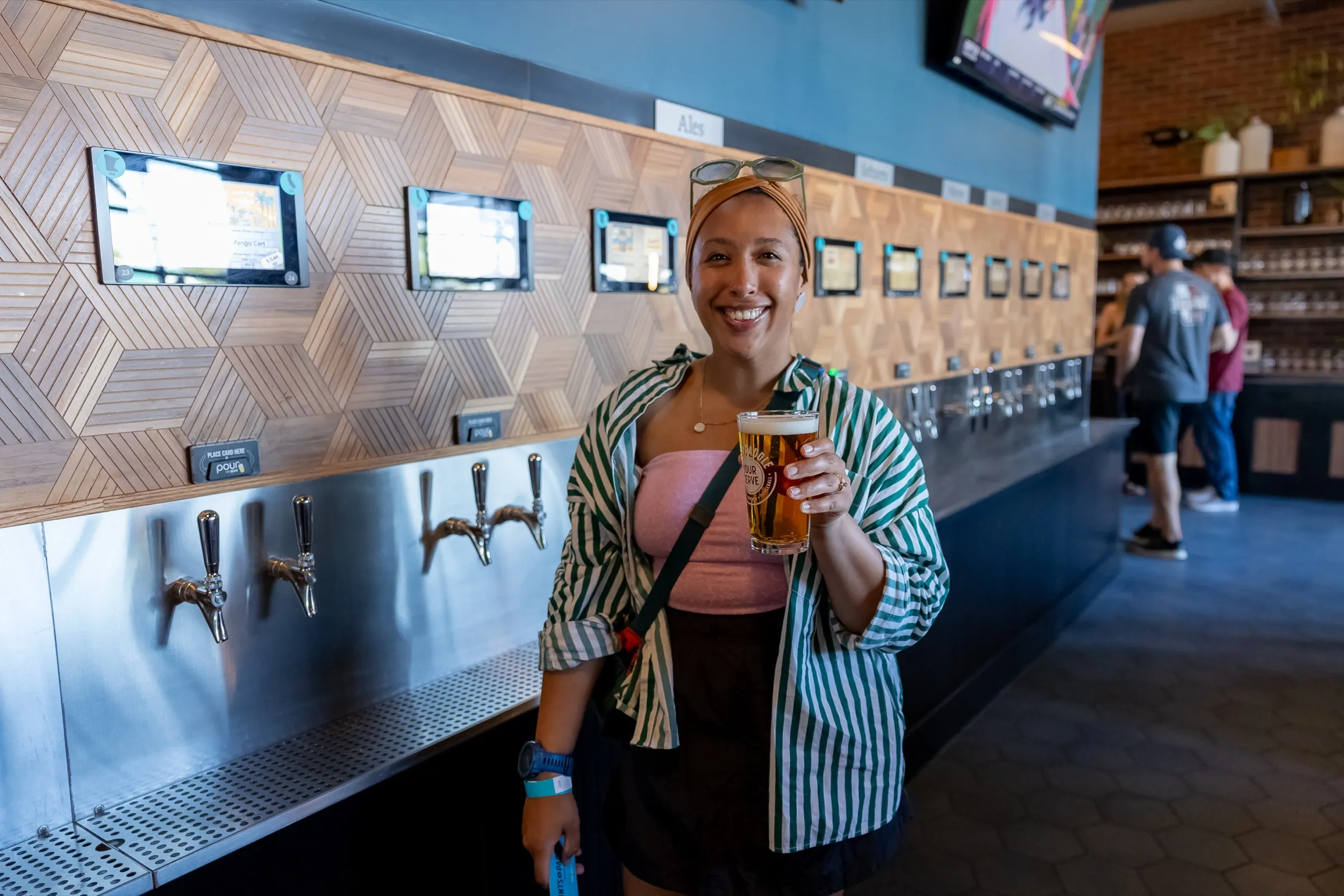 A smiling guest holds up a full pint in front of the self-serve tap wall